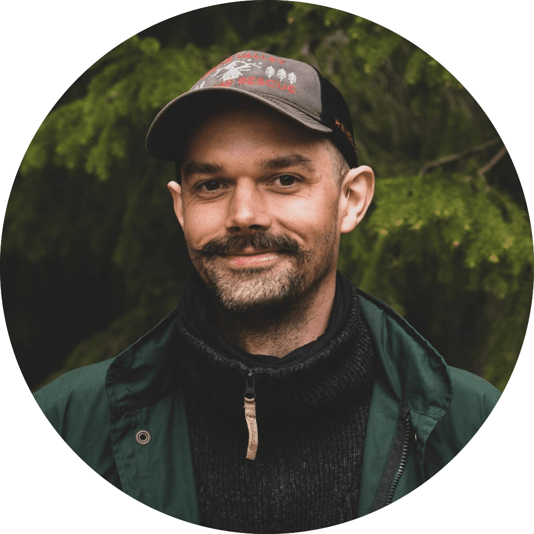 Alvar is wearing a grey hat, a thick wooly jumper and a green jacket. He has a moustache and is smiling.